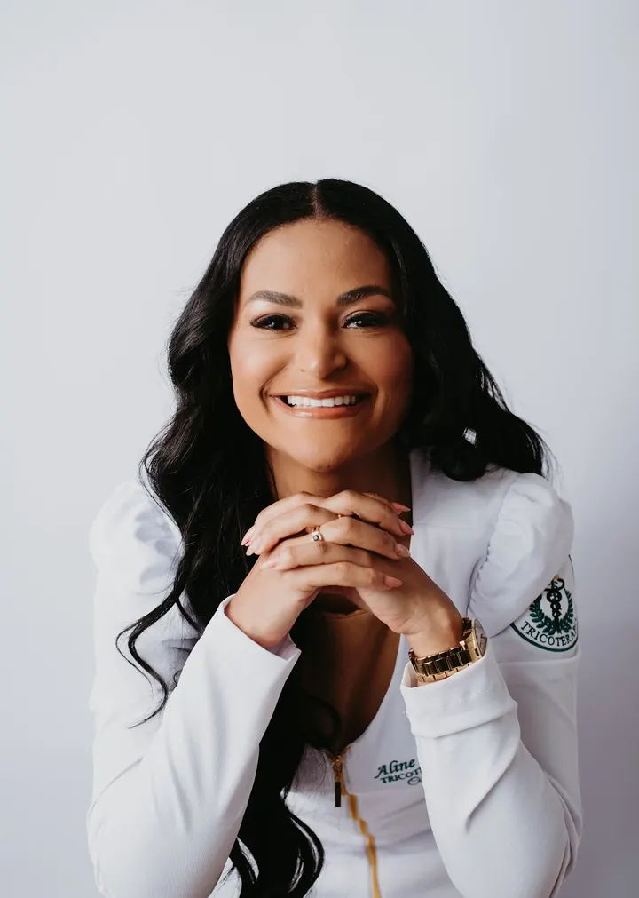 Aline Santos de jaleco branco, sorrindo, com as mãos juntas