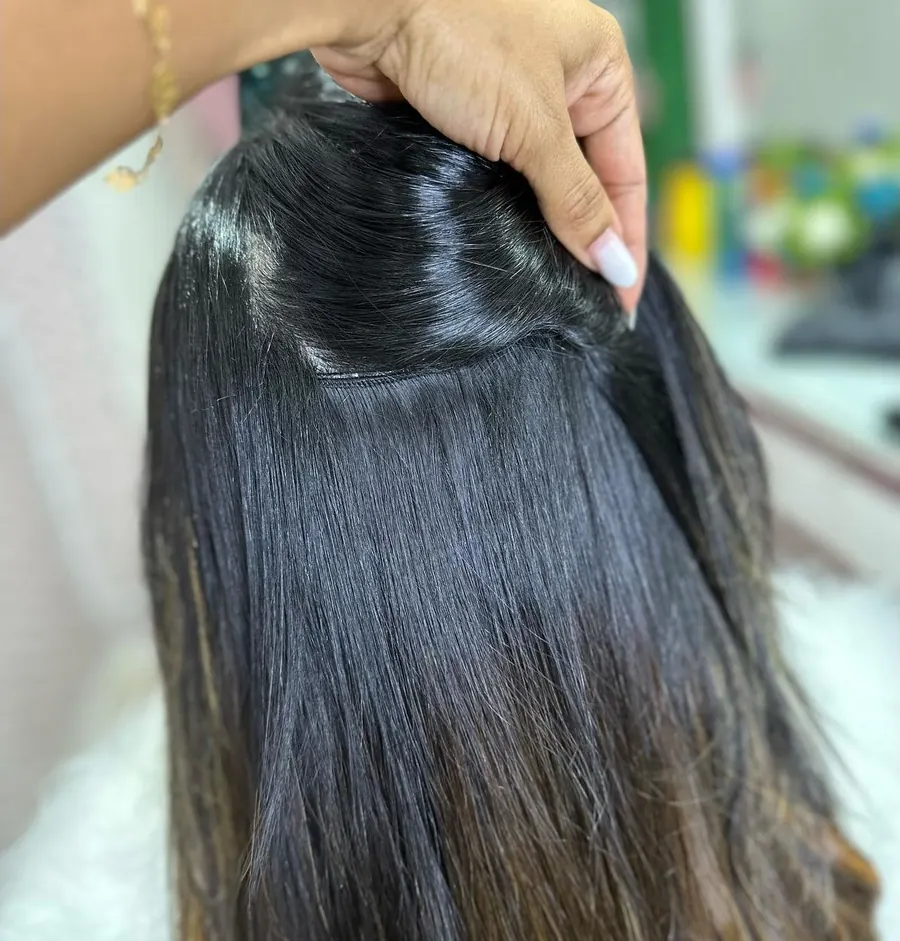 Mão levantando a raiz de um cabelo preto liso, mostrando a aplicação rente ao couro cabeludo