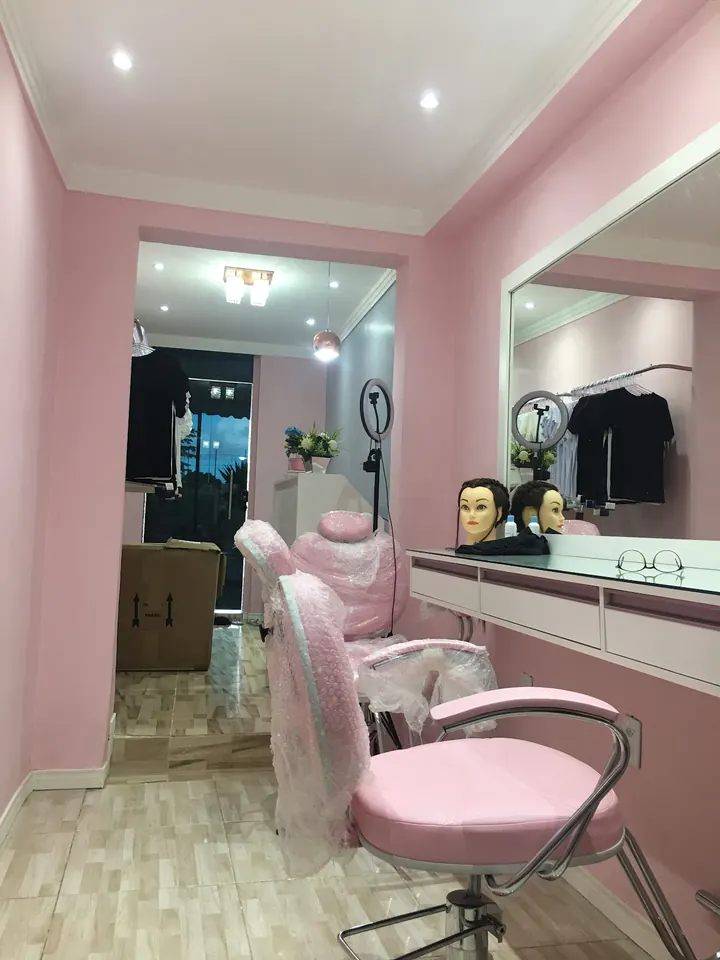 Interior do studio: paredes rosa, espelho grande, bancada branca e cadeira rosa de atendimento